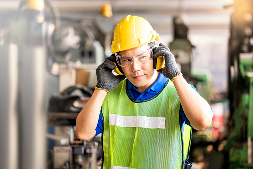 A worker in an industrial or machining profession wears protective gear, particularly hearing protection, while on the job.