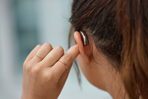 Young woman touches her ear to adjust her hearing aid. It sits discreetly behind her ear.